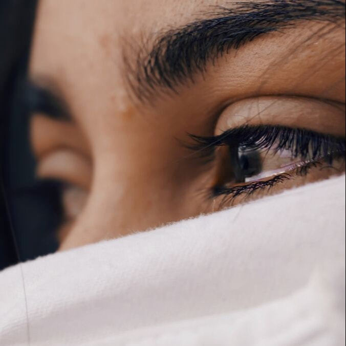 A woman looking far away with tears in her eyes, covering the rest of her face with a white cloth