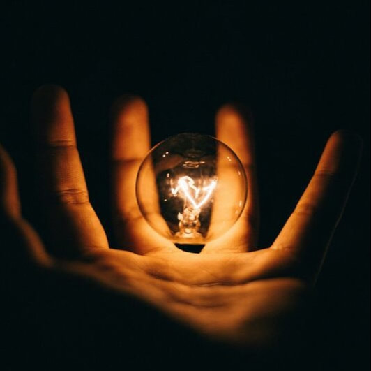 A person's hand holding a floating, illuminated lightbulb