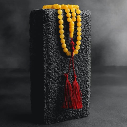 Yellow mala beads with a red thread and tassels placed on top of a rough gray siva lingam.