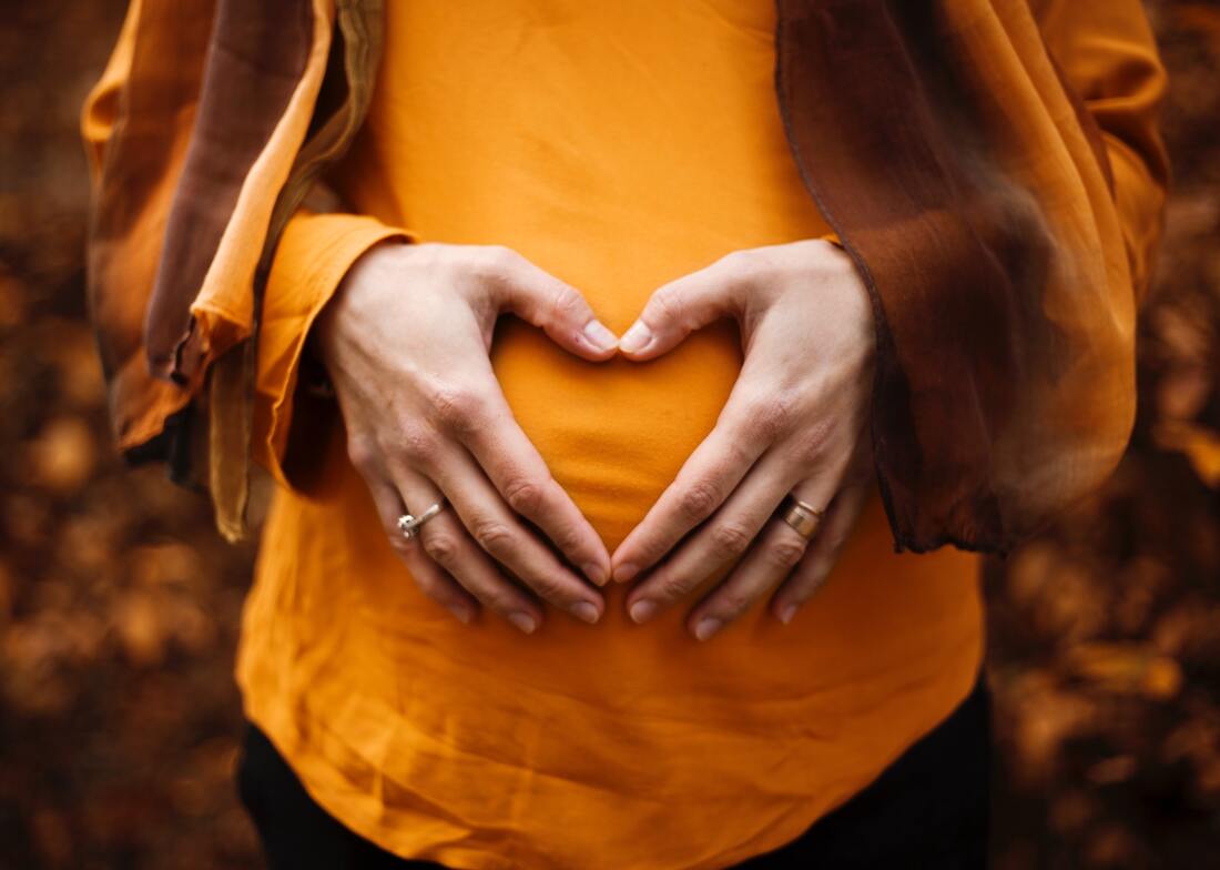 a woman holding her hands in a heart over her pregnant belly