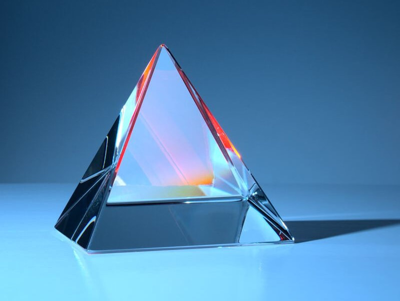 A crystal prism reflecting red, orange and blue light in front of a pale blue background