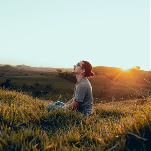 A man meditating in a field at golden hour.