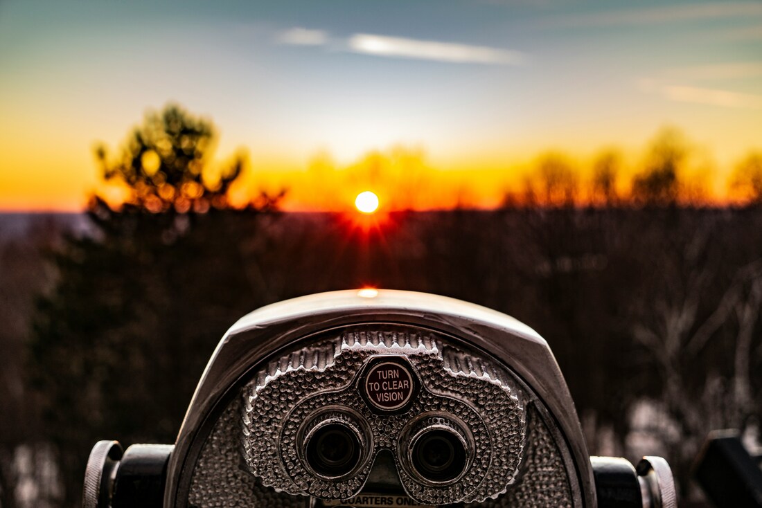 A set of in-ground binoculars stands looking out at the sunset over a rugged landscape